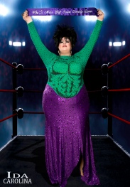 Ida Carolina in a dress that look like the Incredible Hulk holding her Miss Gulf Coast Comedy Queen 2019 sash above her head like a prize fighter.